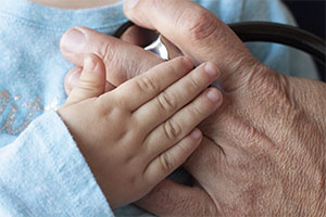 A child's hand rests on the doctor's hand holding the stethoscope to their chest.