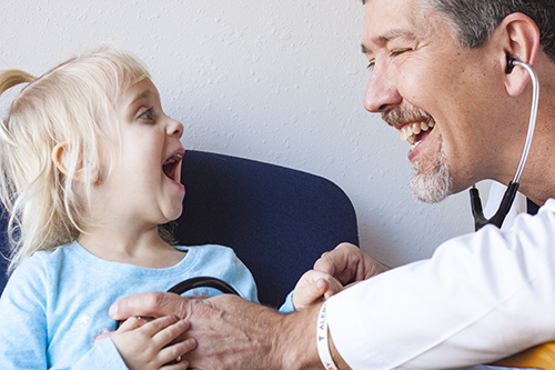 Dr. John smiles as he listens to a young girl's heartbeat.