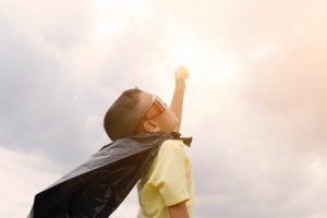 A young boy dressed as a super hero, reaches for the sky.