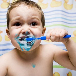 A child has toothpaste all over his mouth as he brushes his teeth.