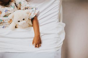 A sick child in bed with their teddy bear.